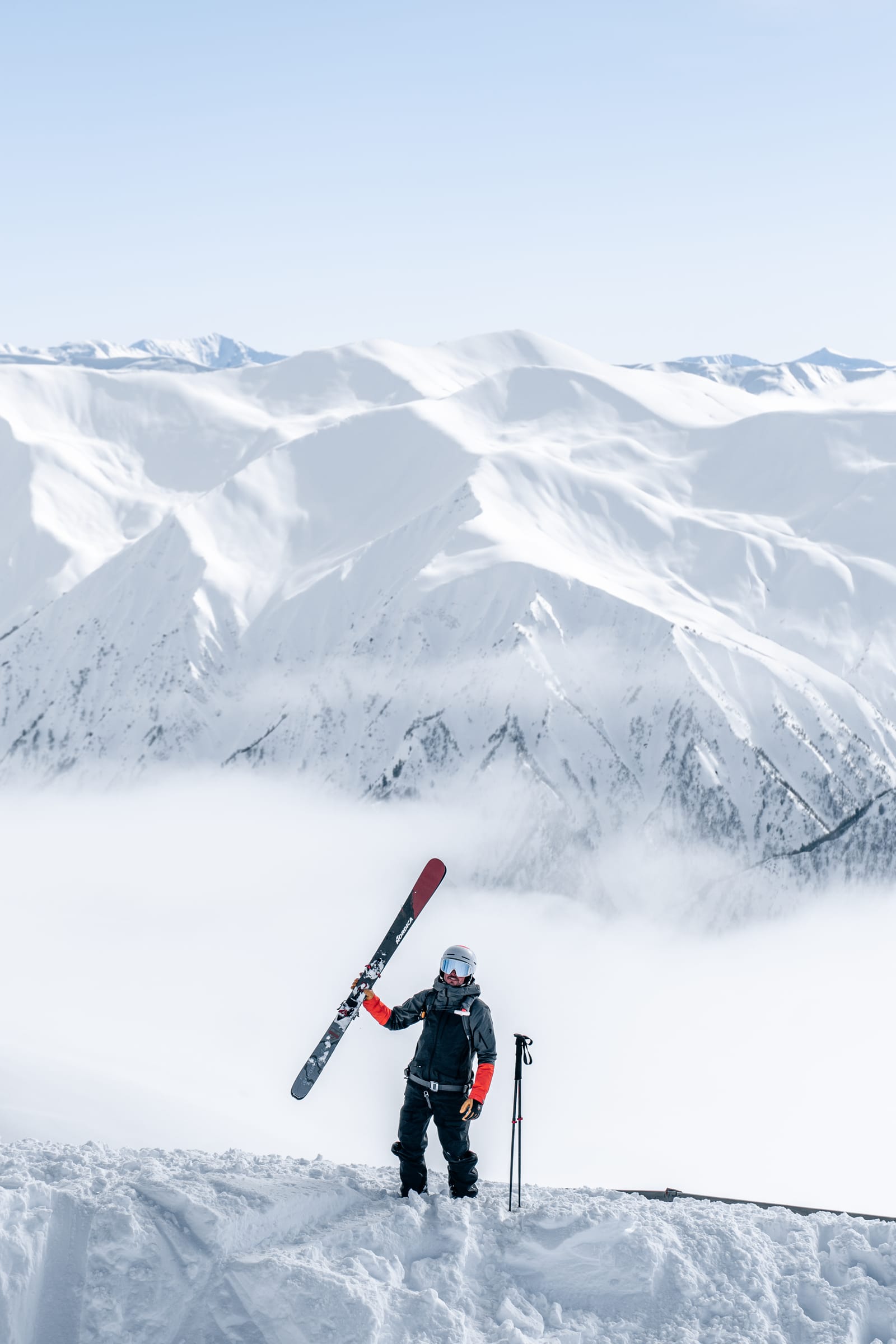 A skier holding a ski upright above snow-covered mountains in Svaneti