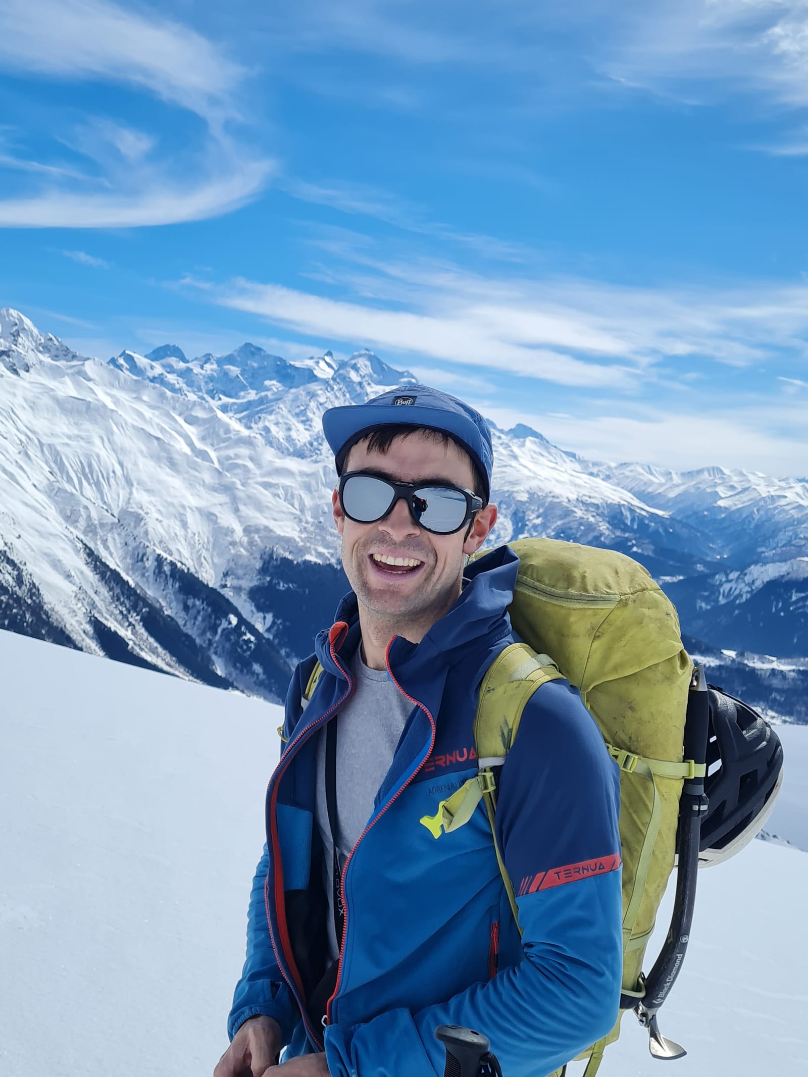 A smiling ski tourer with a backpack on a snowy slope in front of the Svaneti mountain range